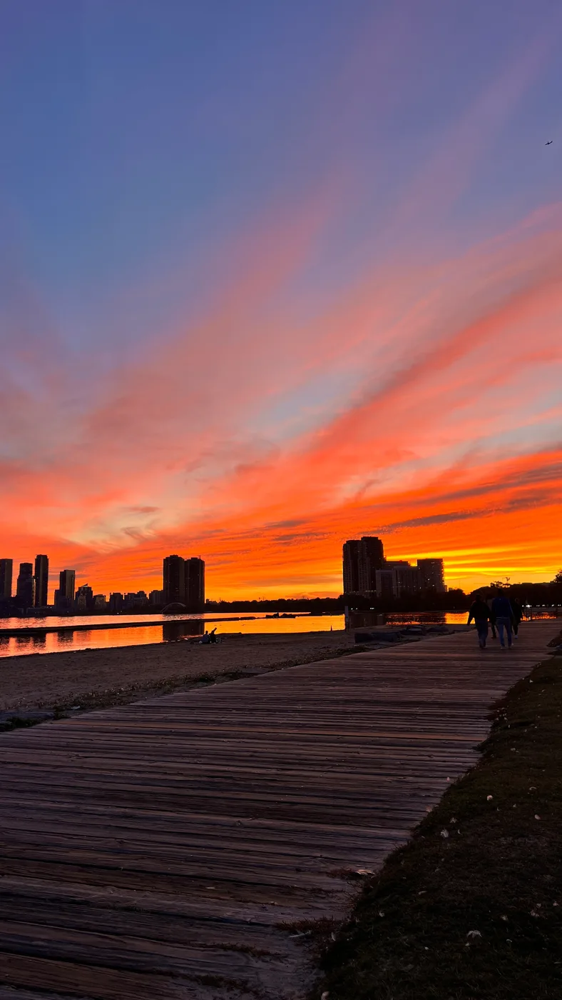 An orange sunset over the Toronto skyline from a lakeside boardwalk